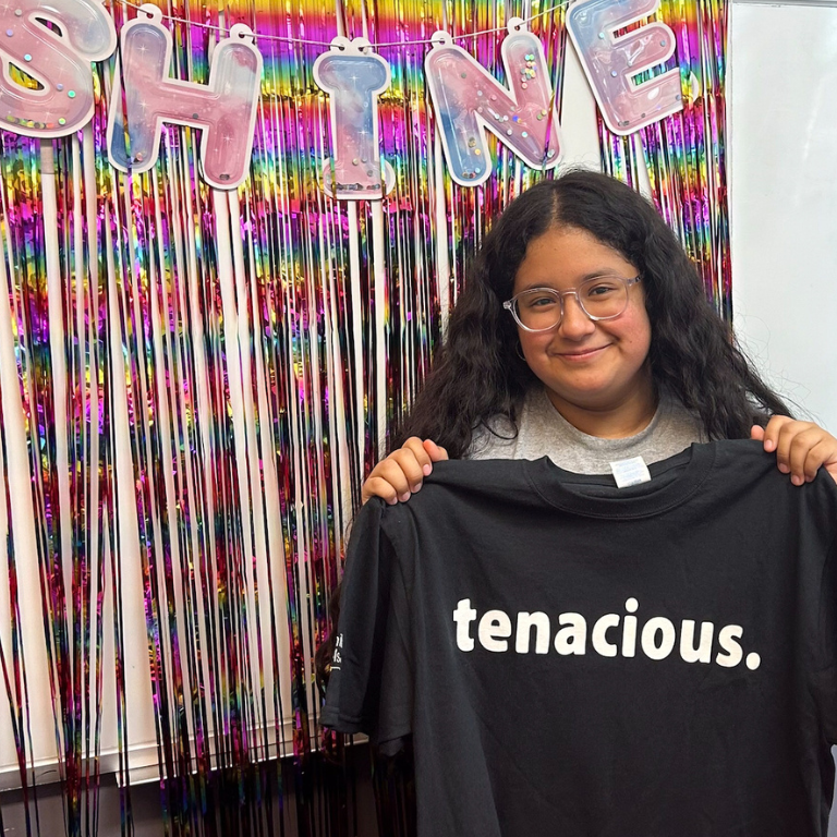 Tenacity Award winner holds up "tenacious" T-shirt