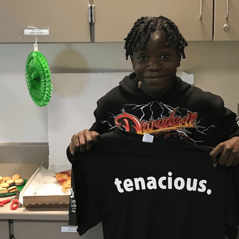 Tenacity Award winner holds up "tenacious" T-shirt